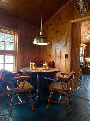 A wooden interior with a round table, four chairs, and a hanging light fixture.