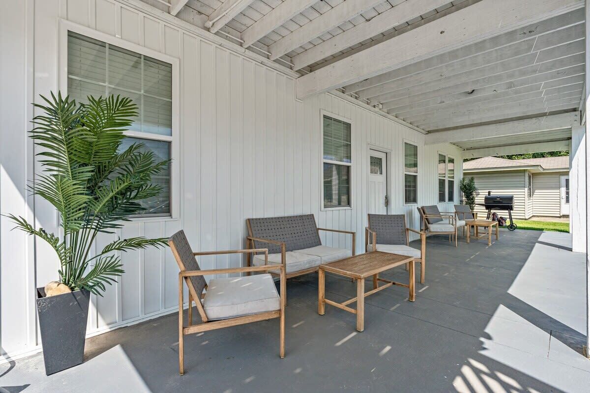 A covered patio with wooden furniture, a potted plant, and a grill in the background.