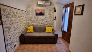 A cozy room with a stone wall, a brown sofa with yellow cushions, and a framed picture above it.