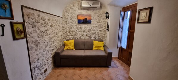 Une pièce chaleureuse avec un mur en pierre, un canapé marron agrémenté de coussins jaunes et un tableau encadré au-dessus.
