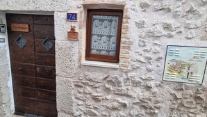 A stone building with a wooden door, a small window with a view of a town, and a sign with the number 74.