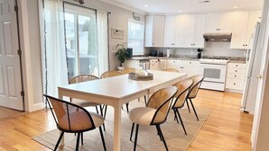 A modern kitchen with white cabinets, a central island, and a dining area with wicker chairs. - Toddler Friendly, toys, boardwalk, beach, downtown, POOL, & clean! You get ALL!  (Point Pleasant Beach)