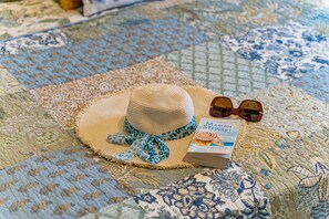 Ein Strohhut, Sonnenbrille und ein Buch auf einer gemusterten Tagesdecke.