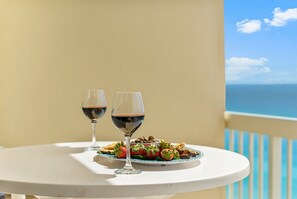 Ein Tisch mit einem Teller Essen und zwei Gläsern Rotwein auf einem Balkon mit Blick aufs Meer.