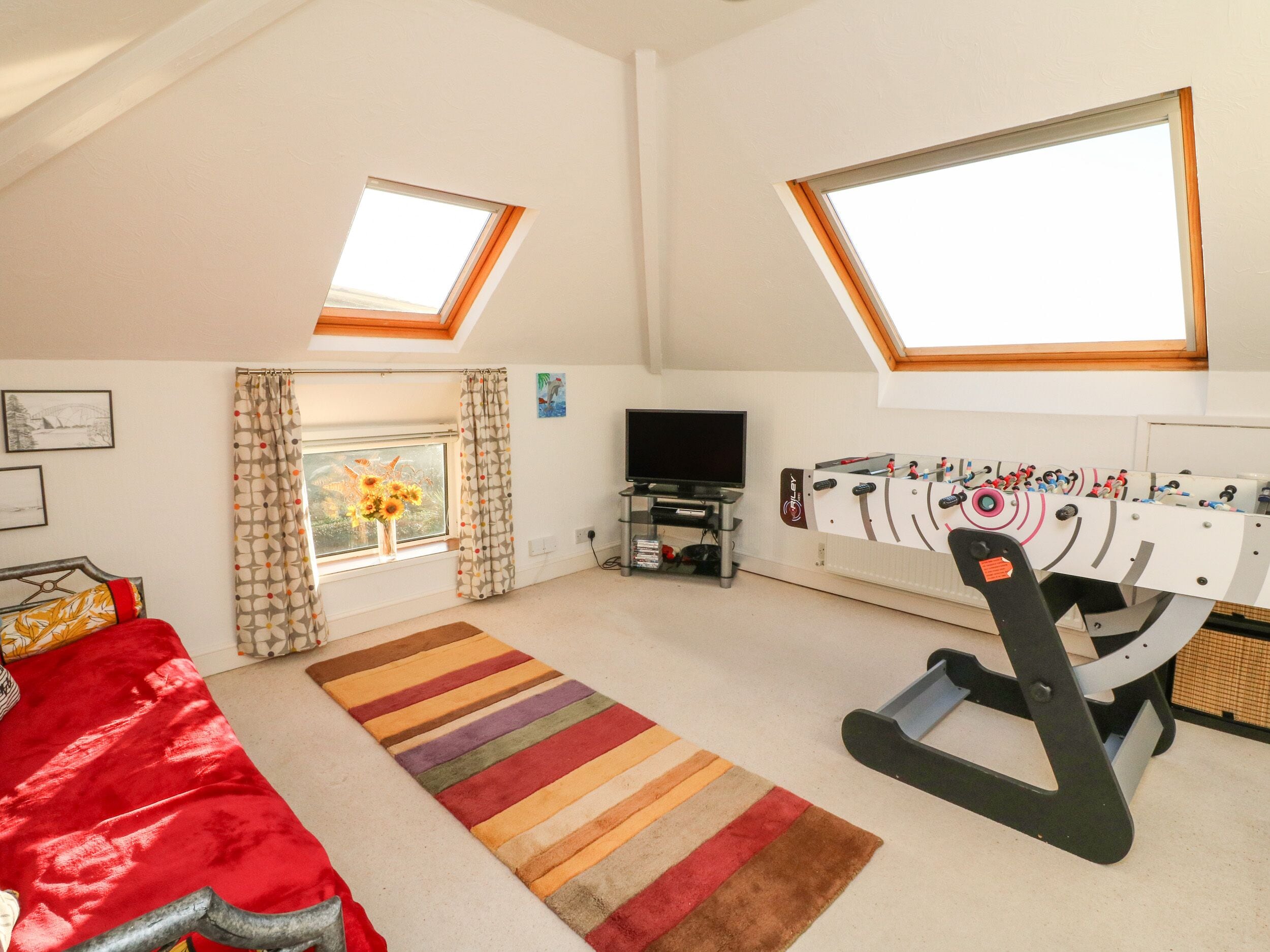 A room with a bed, a TV, a foosball table, and a window with curtains.
