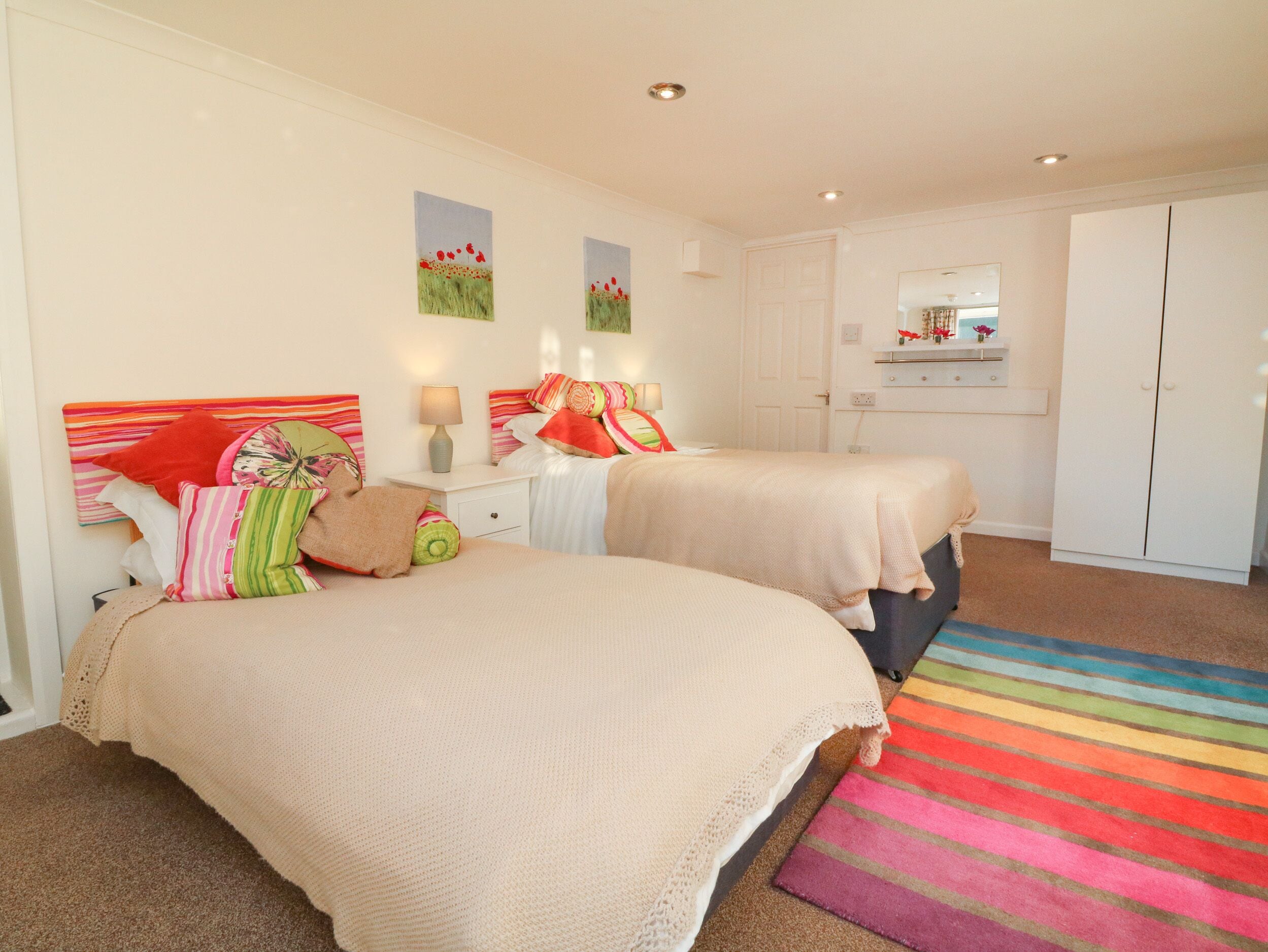 A bedroom with two beds, a colorful striped rug, and a white wardrobe.
