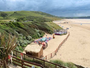 A beach with a fenced area containing a small amusement park, including a carousel and a play structure. - Surf View (Woolacombe)