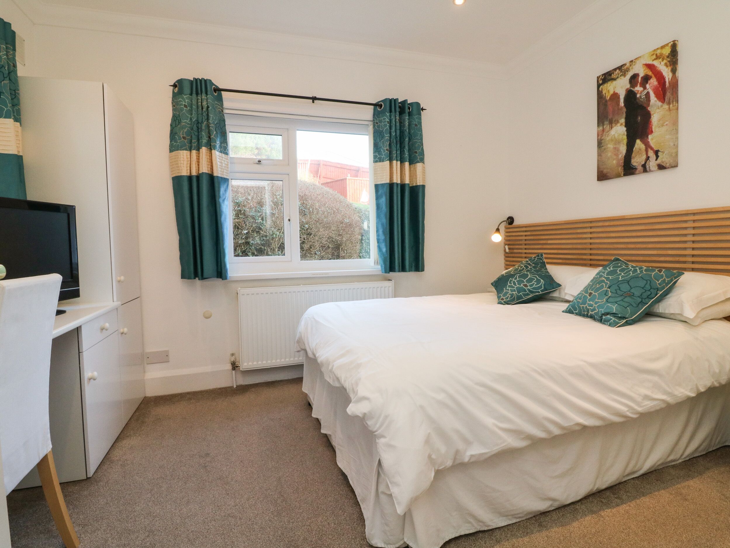 A bedroom with a bed, a desk, a radiator, and a window with curtains.