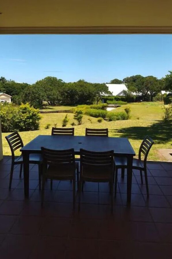 A covered patio with a table and chairs facing a grassy yard with trees and a house in the background. - Exclusive Private Villa Caribbean Estates (Port Edward)