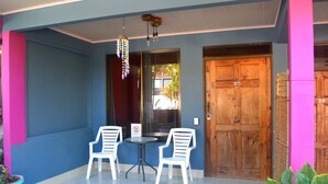 A blue exterior wall, a wooden door with the number 105, and two white plastic chairs with a small table. - White Sands Hotel (Quepos)