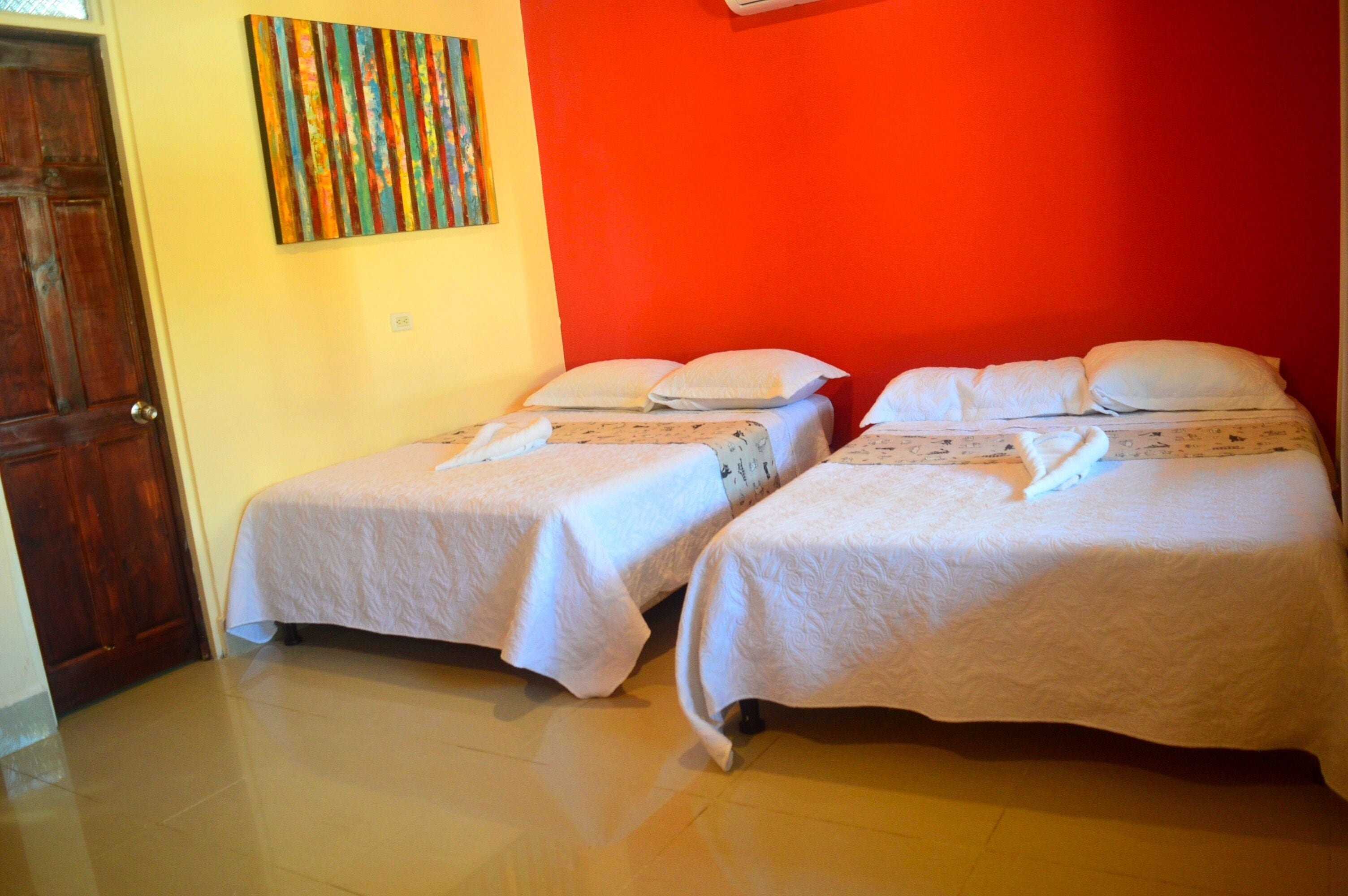 A room with two single beds, a wooden door, and a colorful abstract painting on the wall.