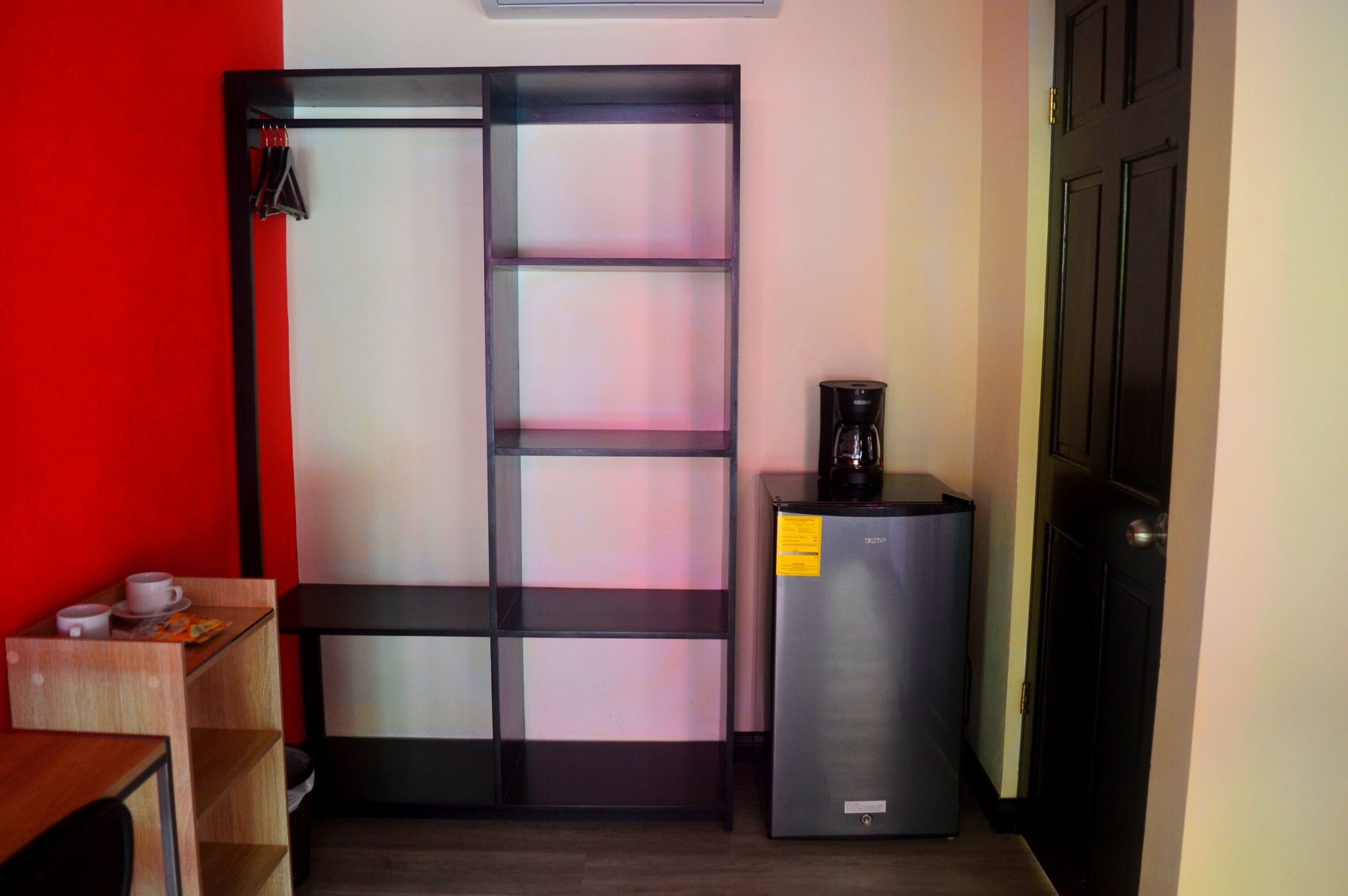 A compact room with a black-framed sliding door, a small table with a cup and saucer, and a refrigerator with a coffee maker.