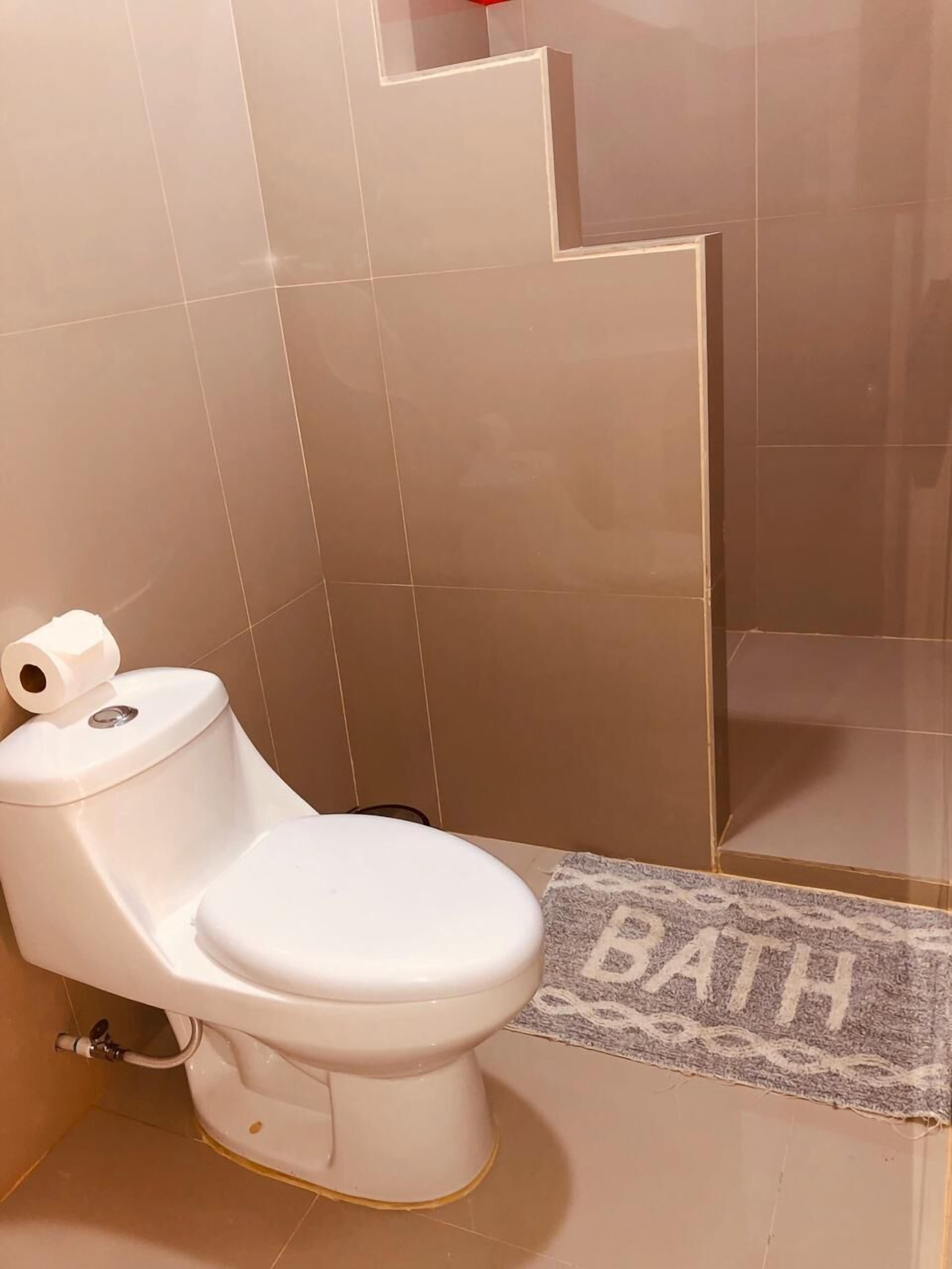 A bathroom with a toilet, a roll of toilet paper, and a rug with the word "BATH" on it.