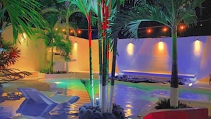 An indoor pool area with lounge chairs, palm trees, and ambient lighting. - White Sands Hotel (Quepos)