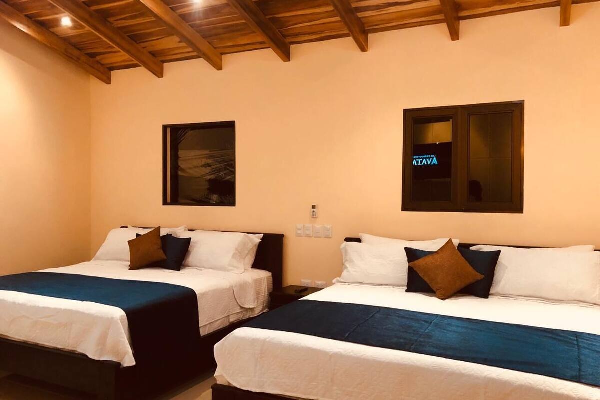 A hotel room with two beds, wooden beams on the ceiling, and a sign for 'ATAVA' on the wall.