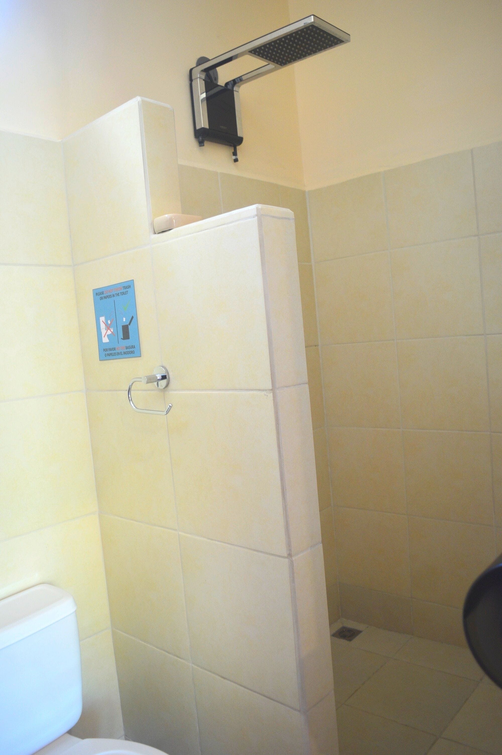 A bathroom with a toilet, a shower stall, and a sign indicating a shared toilet.