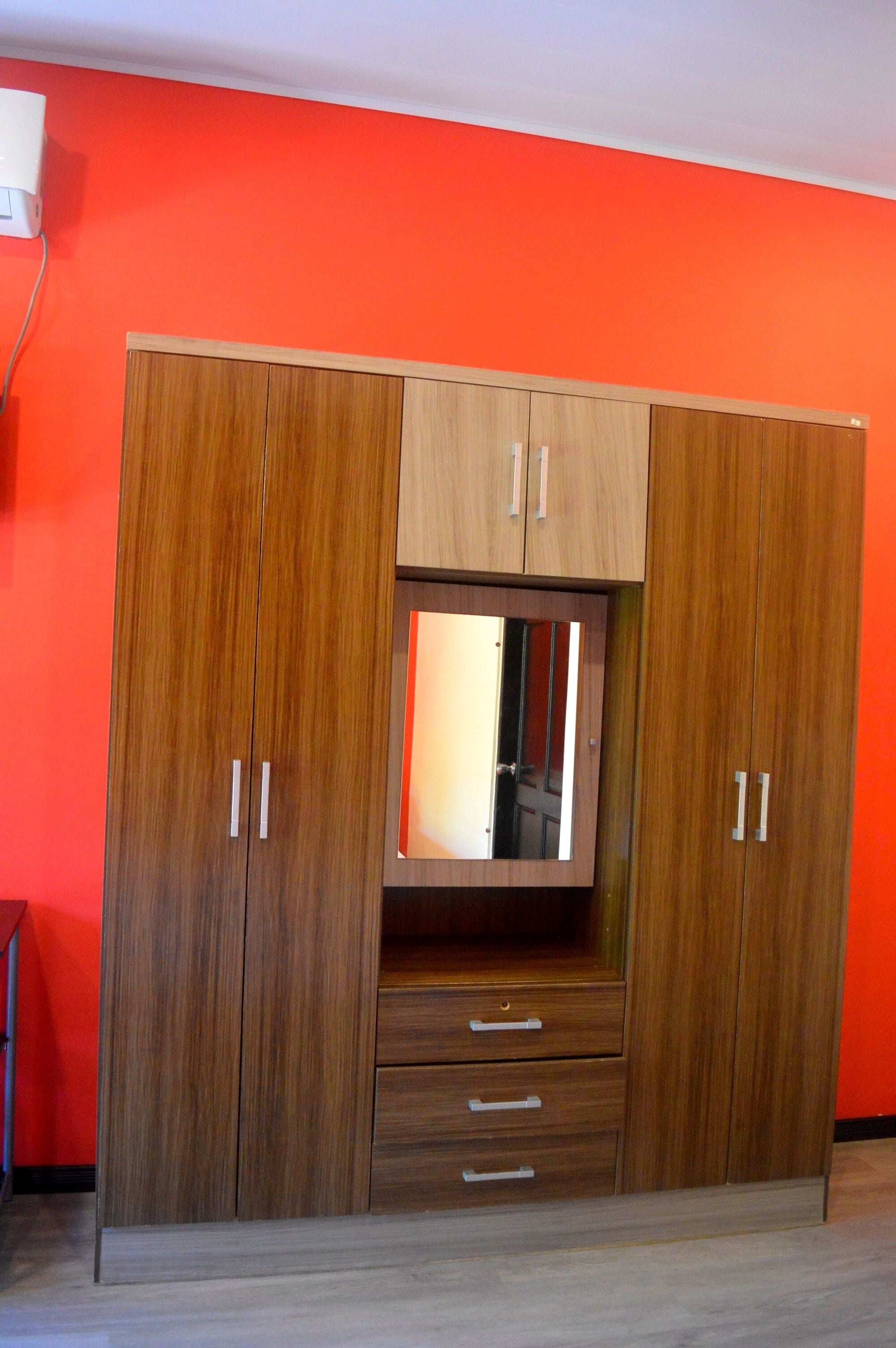 Un armario de madera con dos puertas, un espejo y tres cajones.