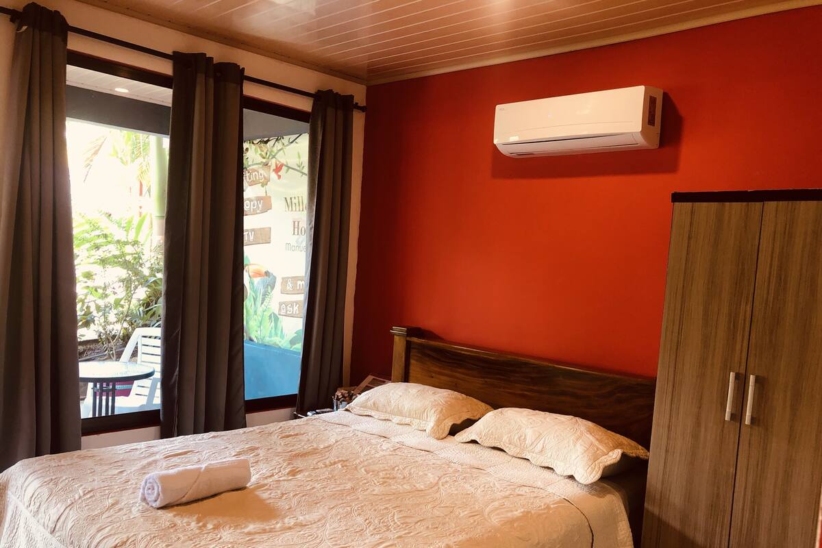 A hotel room with a bed, a wooden wardrobe, and an air conditioning unit on the wall.