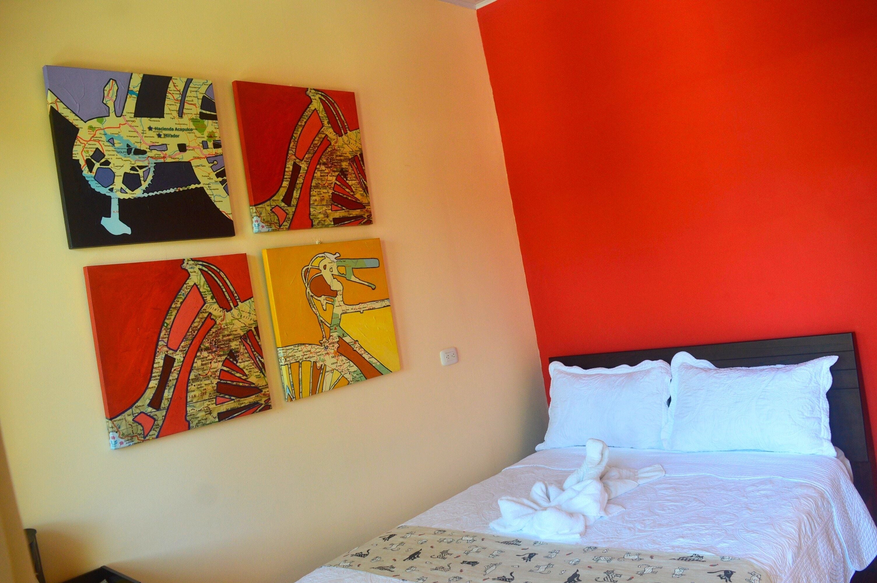 Een hotelkamer met een bed, een rode muur en vier schilderijen aan de muur.