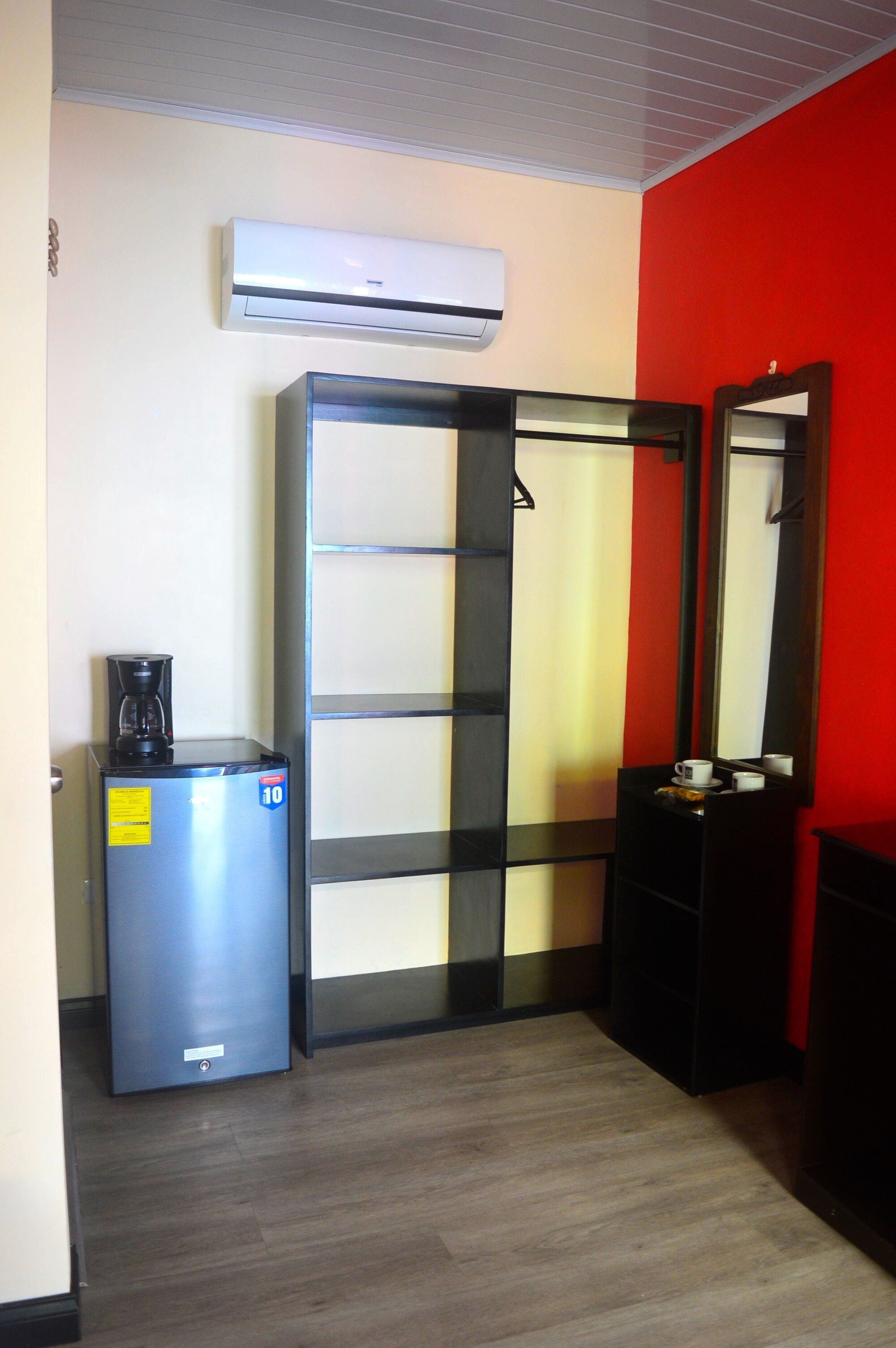 Una habitación de hotel con minibar, cafetera, espejo y una pared de acento roja.