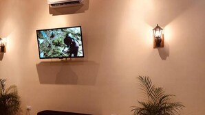 A television mounted on a wall with a wall-mounted air conditioner above it. There are two wall-mounted light fixtures on either side of the television. - White Sands Hotel (Quepos)