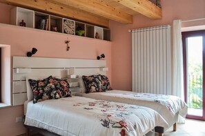 Ein Schlafzimmer mit Holzboden, einem weißen Kopfteil, zwei Betten mit Blumenmuster-Bettwäsche, einem Fenster mit Vorhängen und einem Heizkörper.