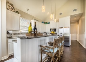 A kitchen with white cabinets, a marble countertop, wicker bar chairs, and hanging pendant lights. - Newly Painted, Luxe 4/4,  Steps to beach, fenced, dog friendly with hot tub (Surfside Beach)