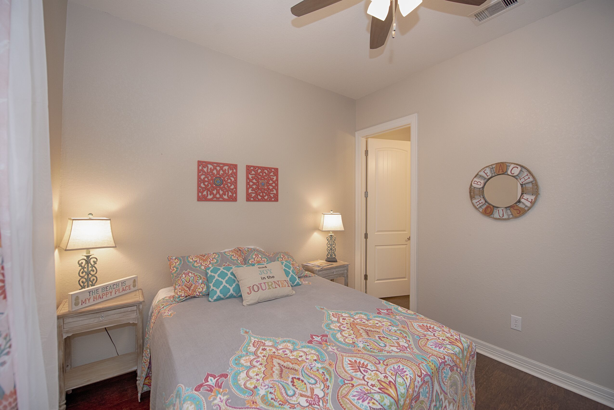 A bedroom with a bed, two nightstands, a ceiling fan, a door, and wall decorations.