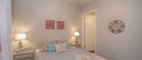 A bedroom with a bed, two nightstands, a ceiling fan, a door, and wall decorations.