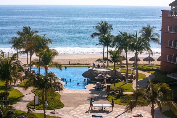A resort with a swimming pool, palm trees, and a beach view.