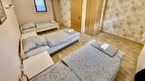 Ein Zimmer mit drei Betten, einem Holzschrank, einem kleinen Fenster und Wandtapete mit Muster.