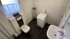 Ein kleines, sauberes Badezimmer mit Toilette, Waschmaschine und Waschbecken.