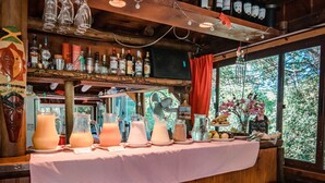 A rustic bar area with wooden shelves holding bottles and glasses, a table with pitchers of drinks, and a chalkboard menu. - Dunas del Este (Punta Colorada)