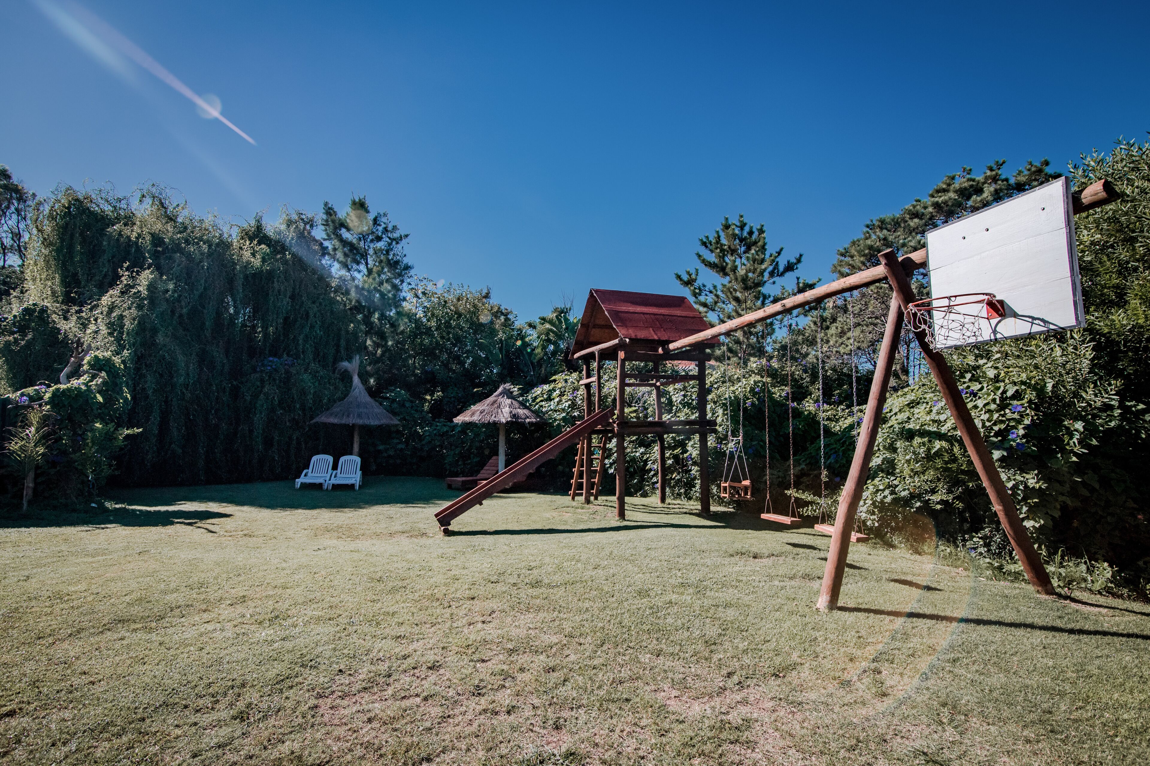 Un parque infantil con columpios, tobogán y un aro de baloncesto.