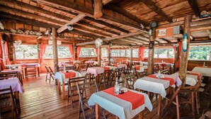 A rustic wooden dining area with tables set for dining, large windows with curtains, and a wooden ceiling. - Dunas del Este (Punta Colorada)