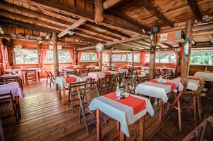 Un comedor rústico de madera con mesas dispuestas para comer, ventanas amplias con cortinas y techo de madera.