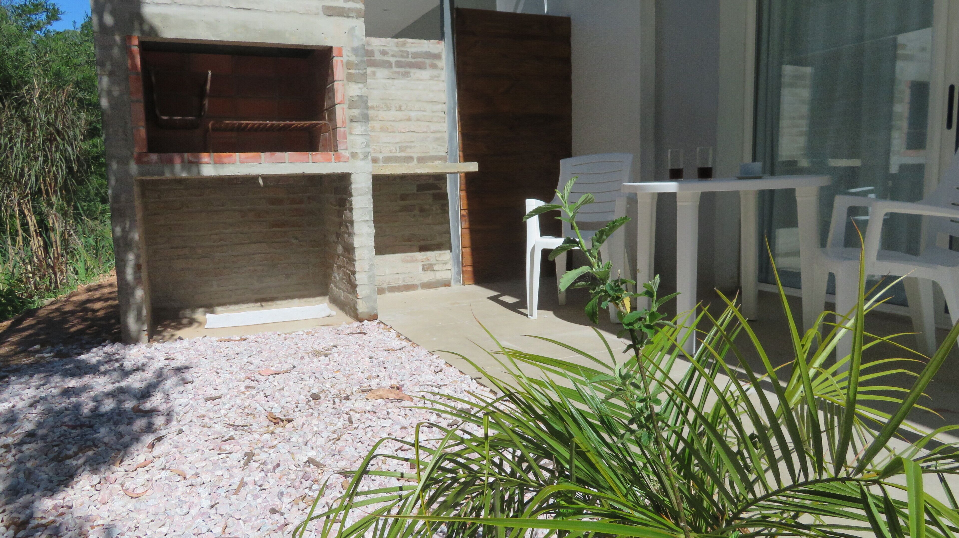 A patio area with a brick fireplace, white plastic chairs, and a gravel ground.