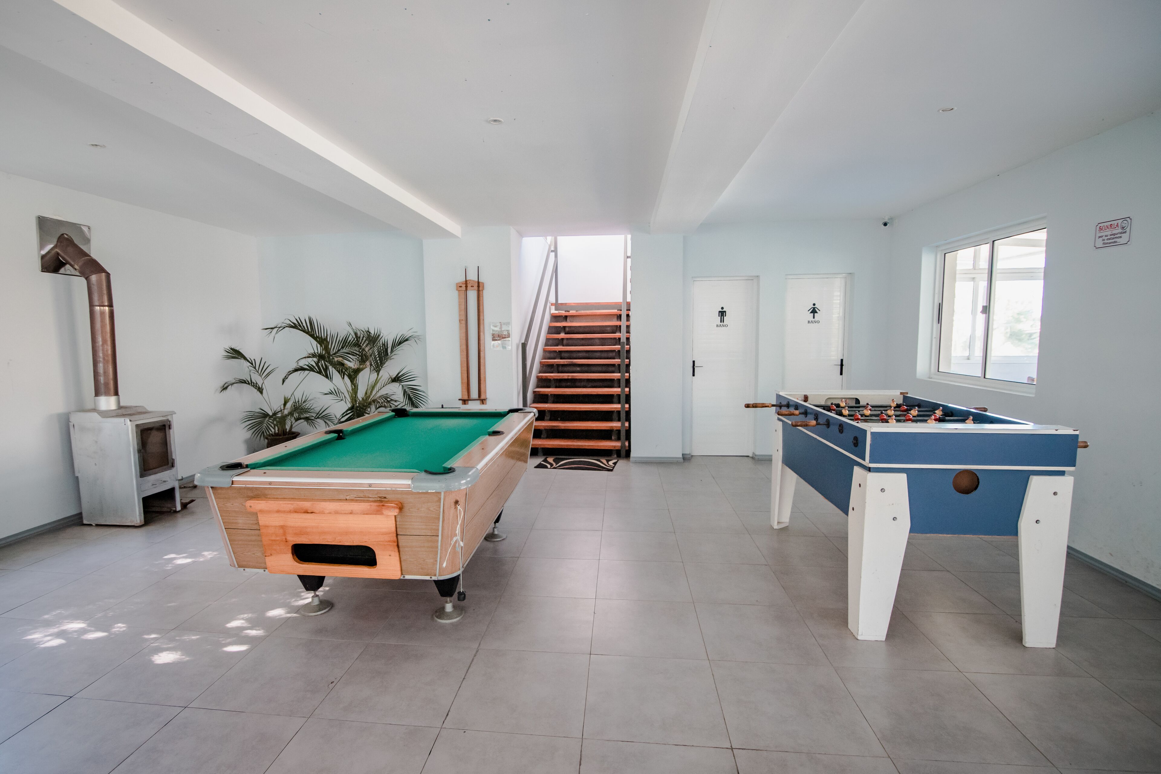Amplia zona de recreación interior con mesa de billar, mesa de fútbol de mesa y una escalera que conduce a un nivel superior.