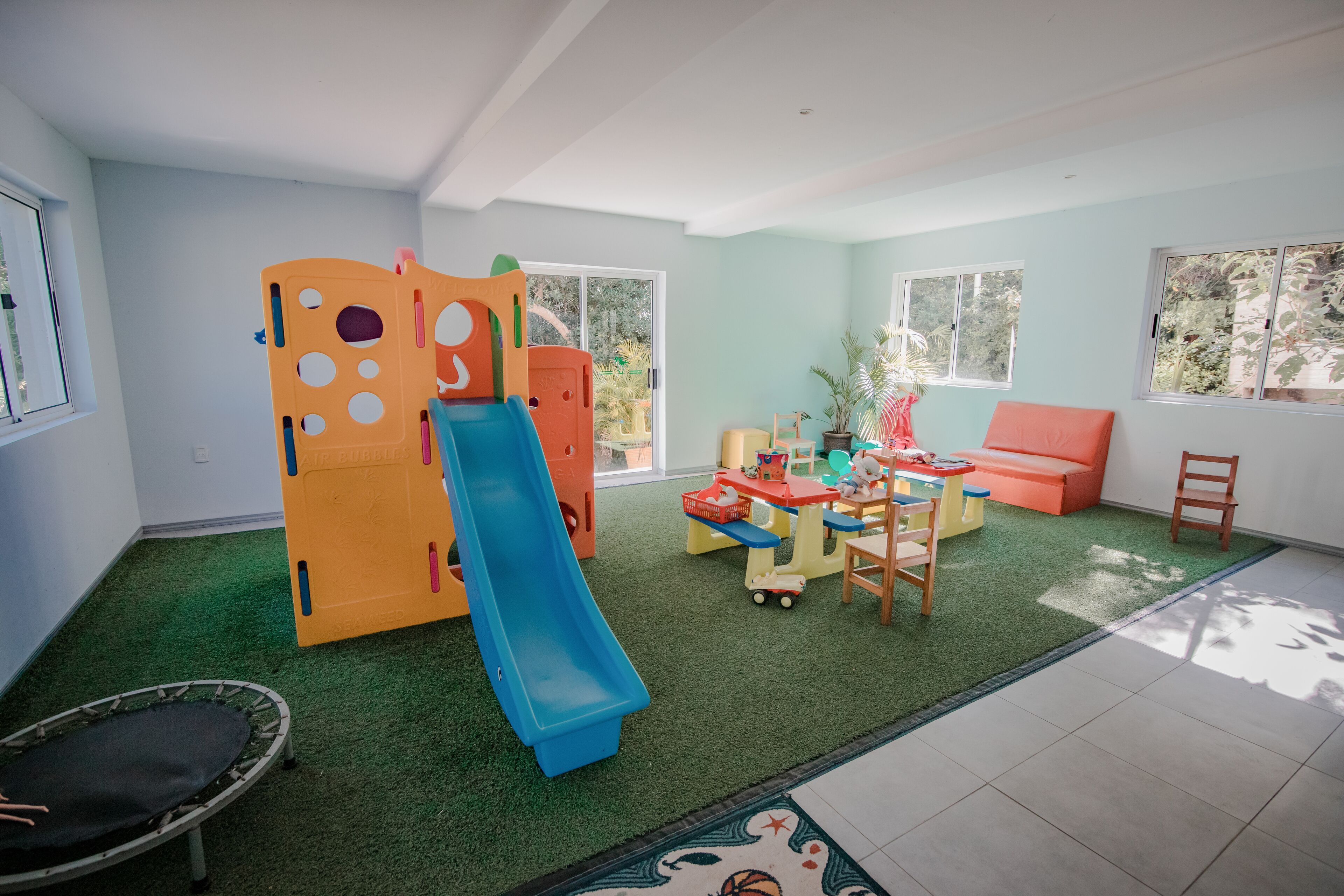 A play area with a slide, play structure, and a small trampoline. There is a sofa and a table with toys.