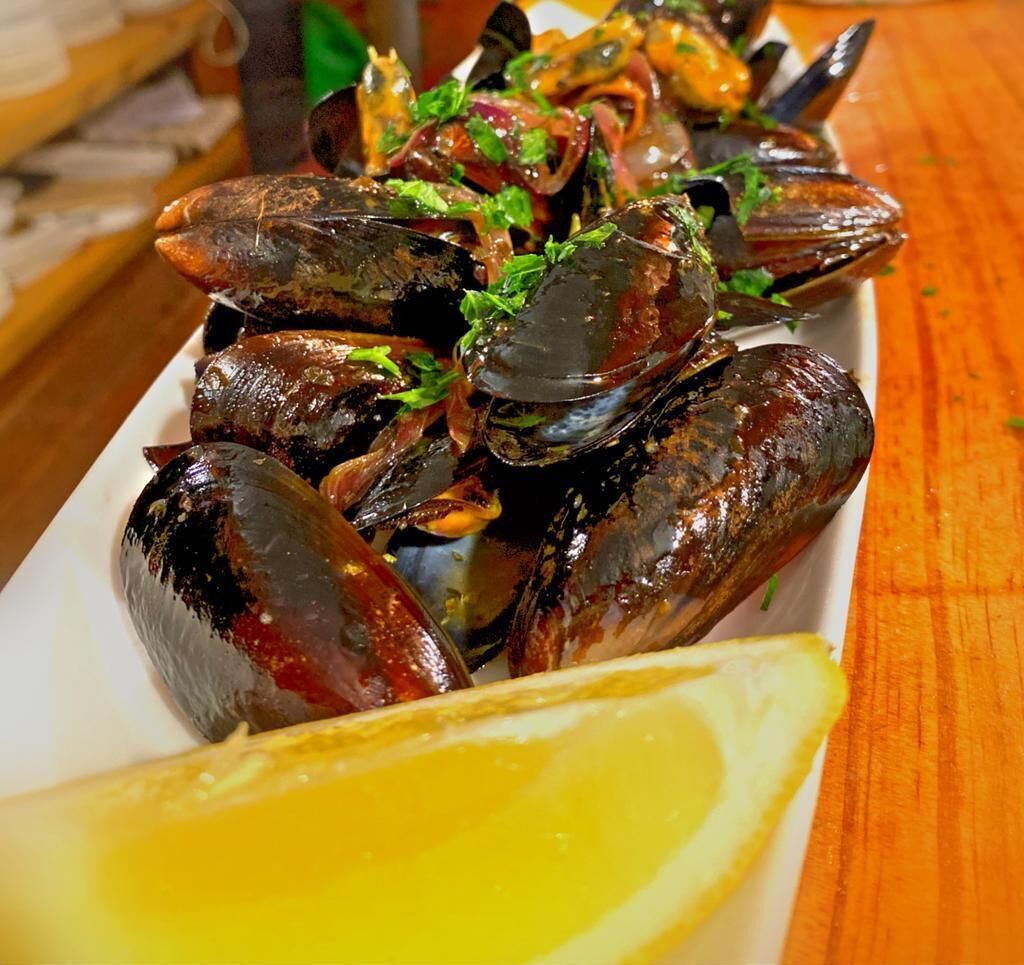 A dish of mussels garnished with herbs and lemon on a white plate.