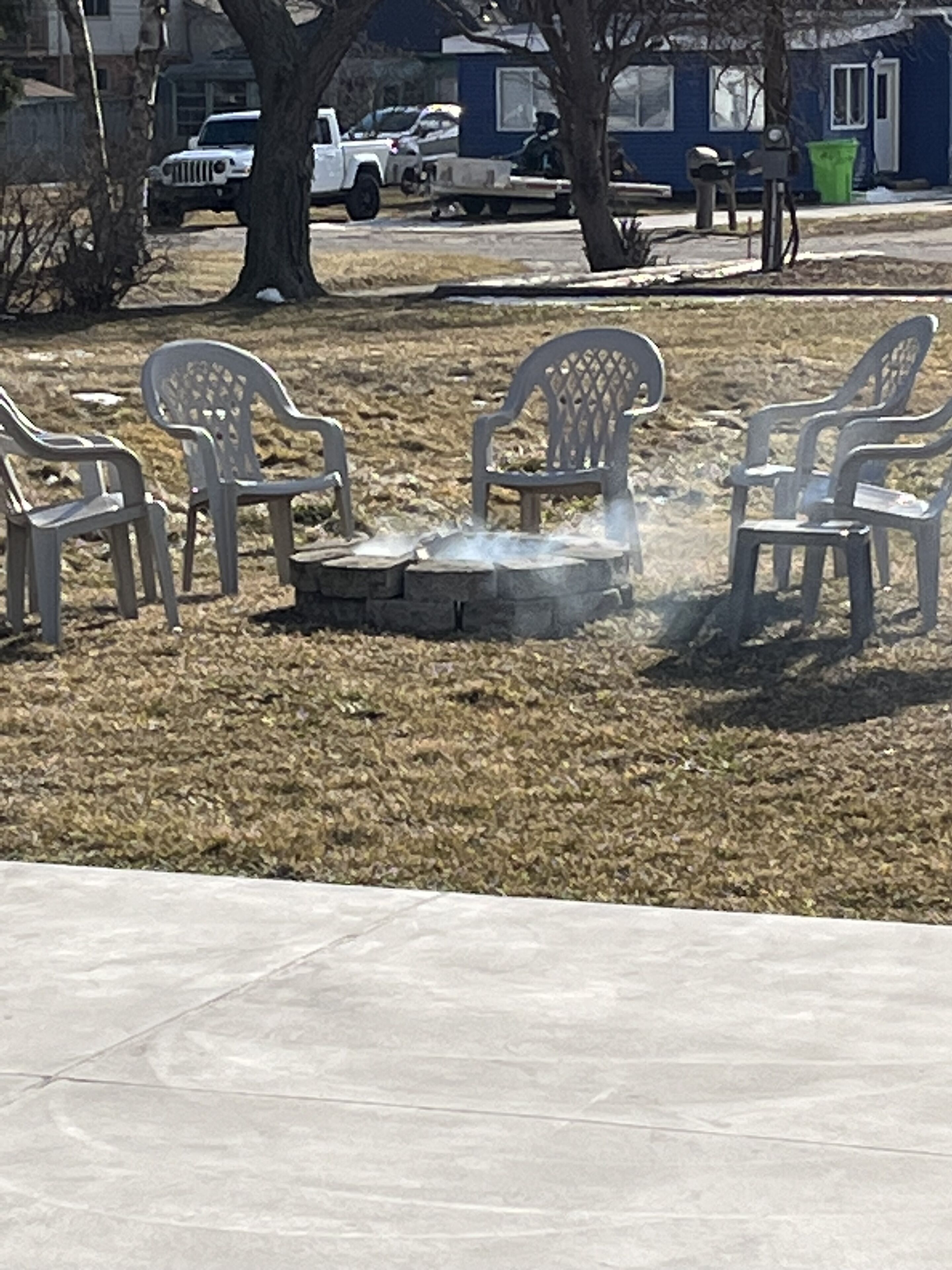 Outdoor plastic chairs arranged around a stone fire pit.