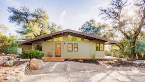 A single-story house with a sloped roof, a front porch, and a gravel driveway. - Hidden Oasis Hot Tub-Disney Train Track. (Julian)