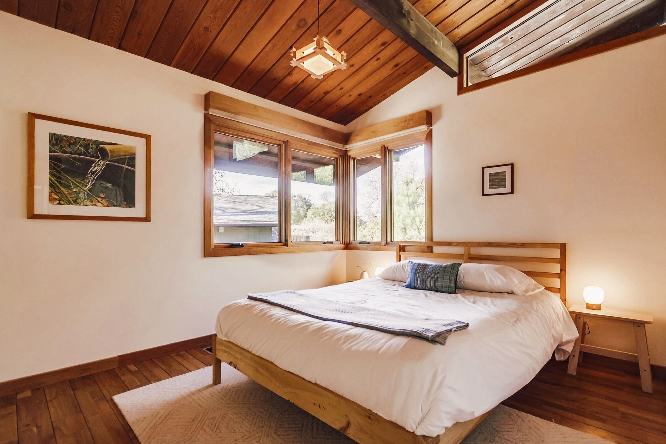 Ein Schlafzimmer mit einem Holzbett, großen Fenstern und einer Deckenleuchte.