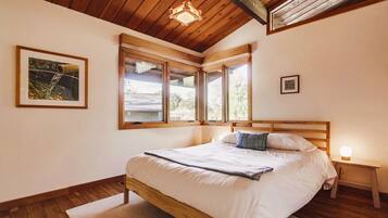 Ein Schlafzimmer mit einem Holzbett, großen Fenstern und einer Deckenleuchte.