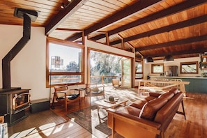 Relax in a spacious living area with a leather sofa, wooden chairs, and dining table, featuring a wood-burning stove and modern kitchen.