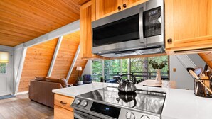 A modern kitchen with wooden cabinets, stainless steel appliances, and a large window offering a view of the outdoors. - Black Butte Ranch A-Frame · Pools, Golf, Sleeps 8 (Sisters)