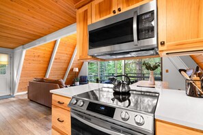 A modern kitchen with wooden cabinets, stainless steel appliances, and a large window offering a view of the outdoors. - Black Butte Ranch A-Frame · Pools, Golf, Sleeps 8 (Sisters)