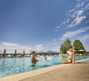 Una piscina con sillas de descanso y sombrillas, rodeada de árboles y una montaña al fondo.