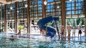 Une piscine intérieure avec un toboggan, de grandes fenêtres et un espace couvert équipé de chaises longues.