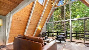 A modern loft bedroom with a sloped ceiling, large windows, and a cozy seating area. - Black Butte Ranch A-Frame · Pools, Golf, Sleeps 8 (Sisters)